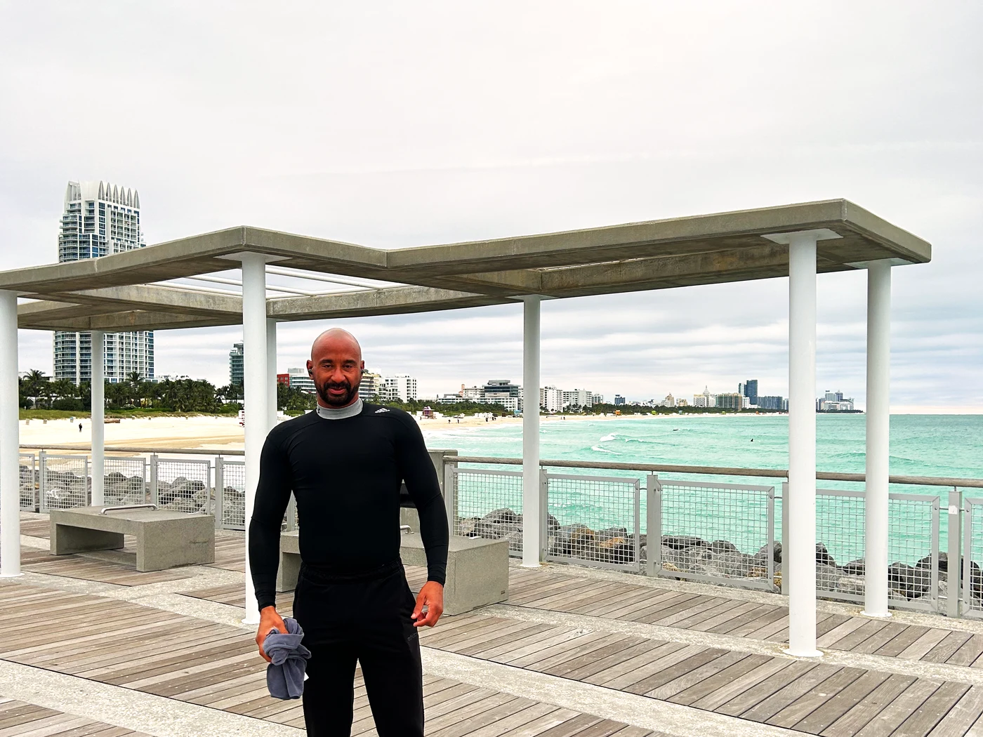 Peter C. Bennett in athletic wear on a boardwalk pavilion with the beach and city skyline behind him