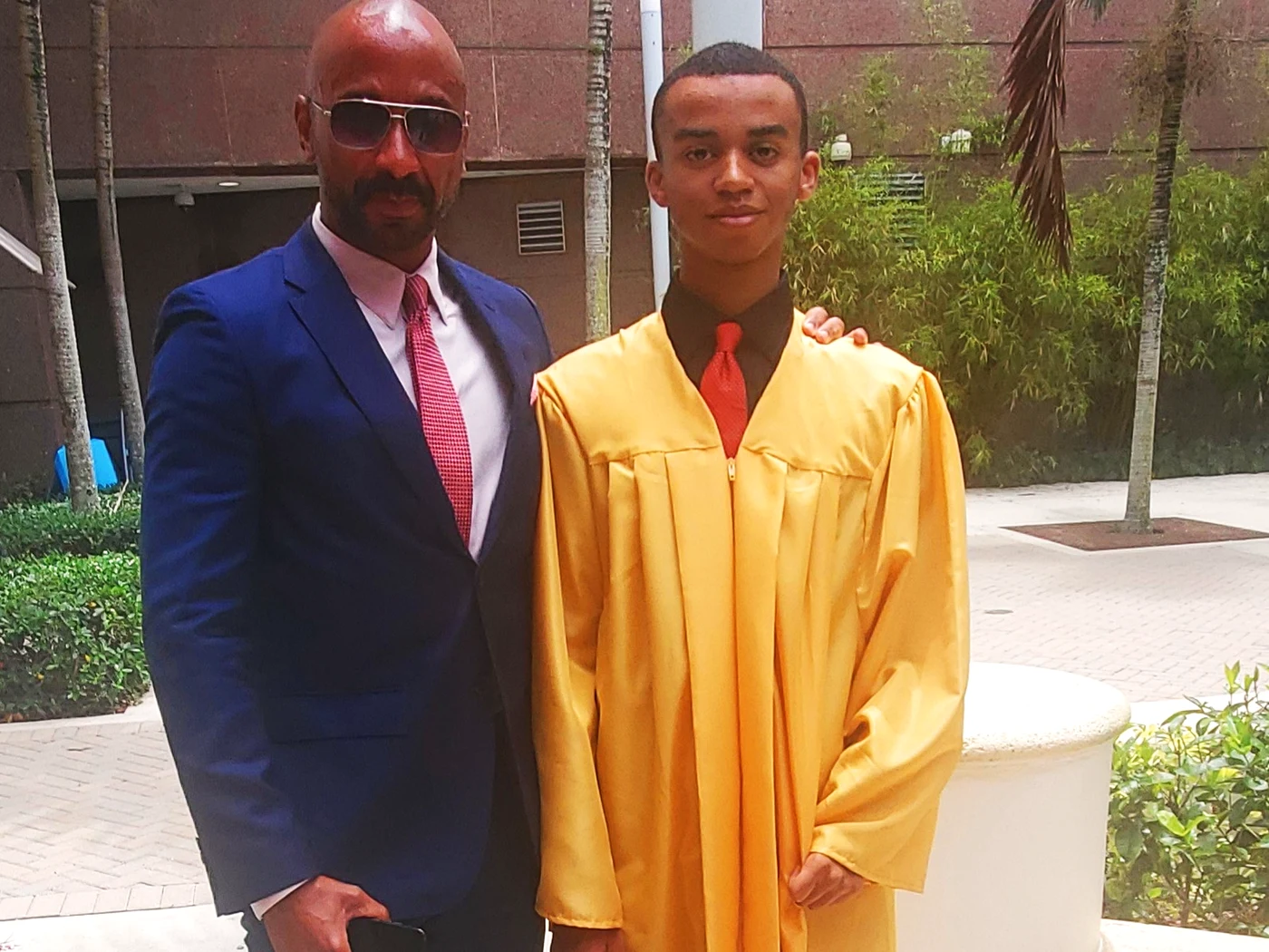 Peter C. Bennett in a suit standing beside a graduate in a gold gown