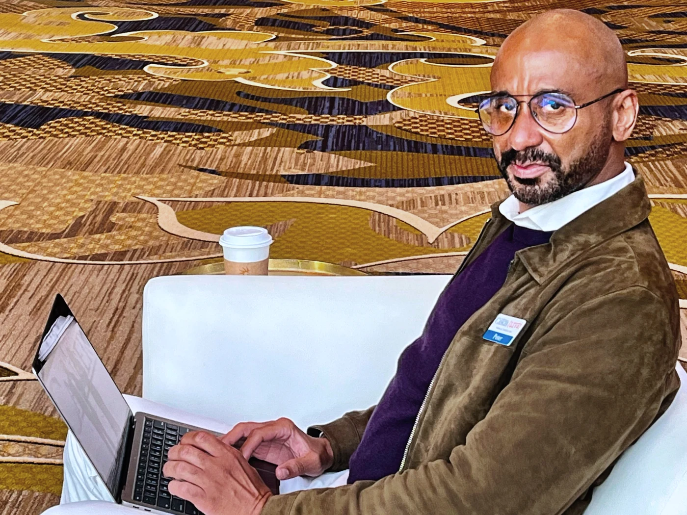Peter C. Bennett seated at a conference table with a laptop, coffee, and a name badge